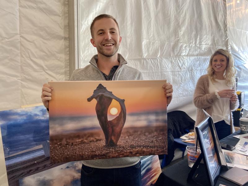 Photographer Elliot MacGuire displays one of his prints on canvas while Alexandra Roberts assists customers.